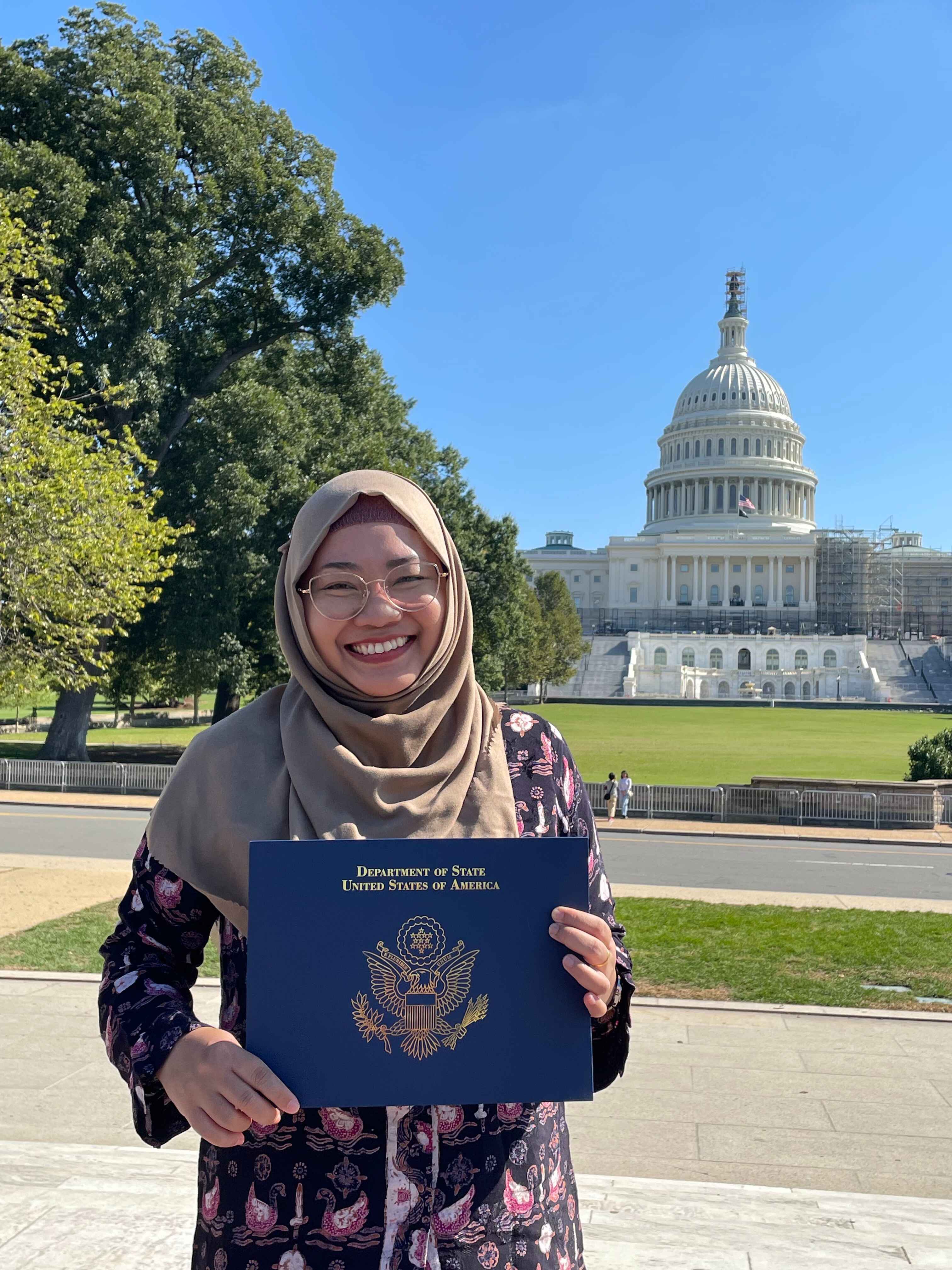 A fellow in Washington DC posing in front of the Capitol building with their diploma